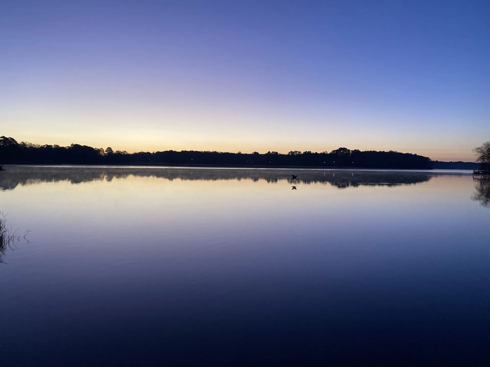 Deep blue twilight over a glassy private lake, the tree line silhouetted against a fading gold horizon