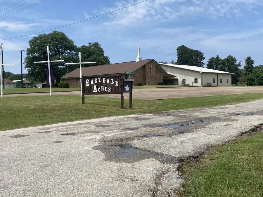 The rustic wooden Eastdale Acres community sign beside the road, with the neighborhood church building behind it